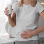 Frau mit Glas Milch hält sich den Bauch als Symbol für Nahrungsmittelunverträglichkeit